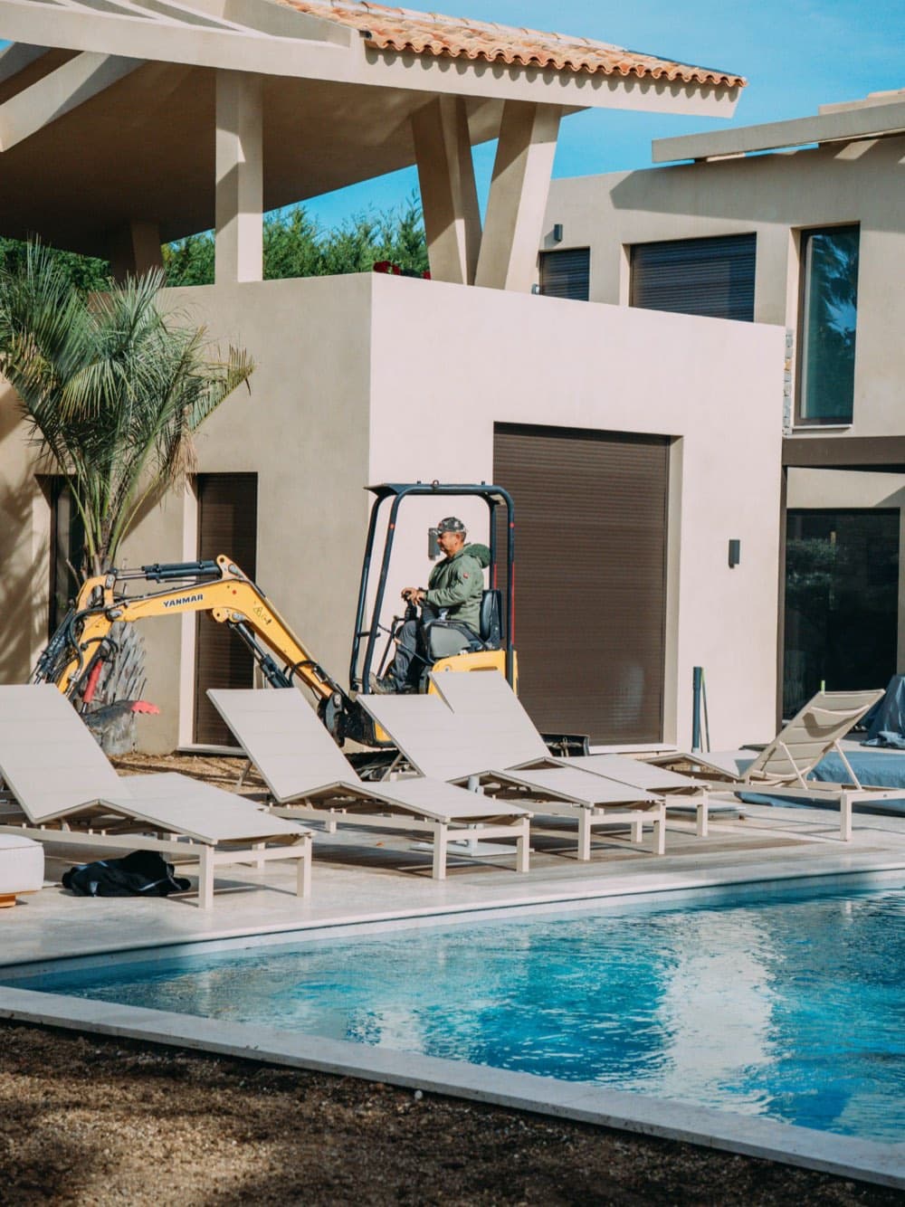 Mini-pelle de BML Paysages entre les transats d’une villa avec piscine, pendant l’aménagement du jardin à Ramatuelle