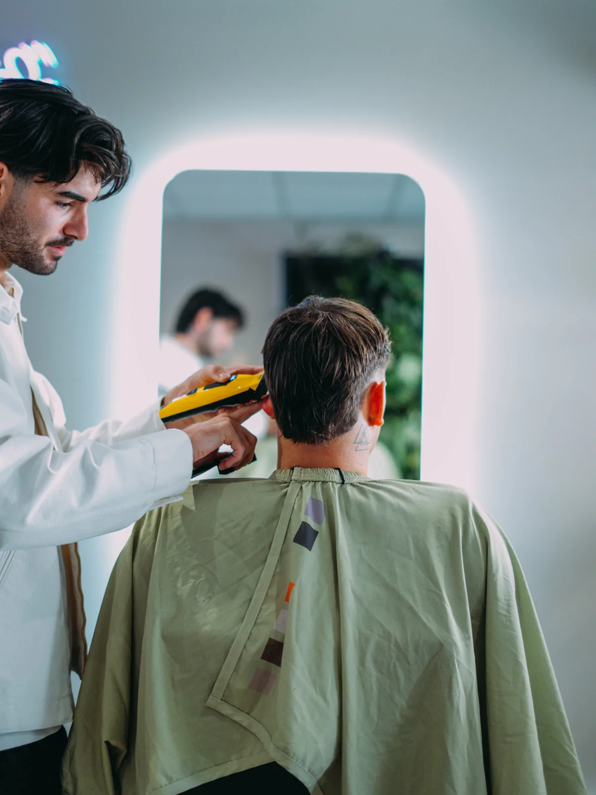 Un barbier des Barbiers du Port coupe les cheveux d’un client à la tondeuse devant le miroir lumineux du salon de Carqueiranne